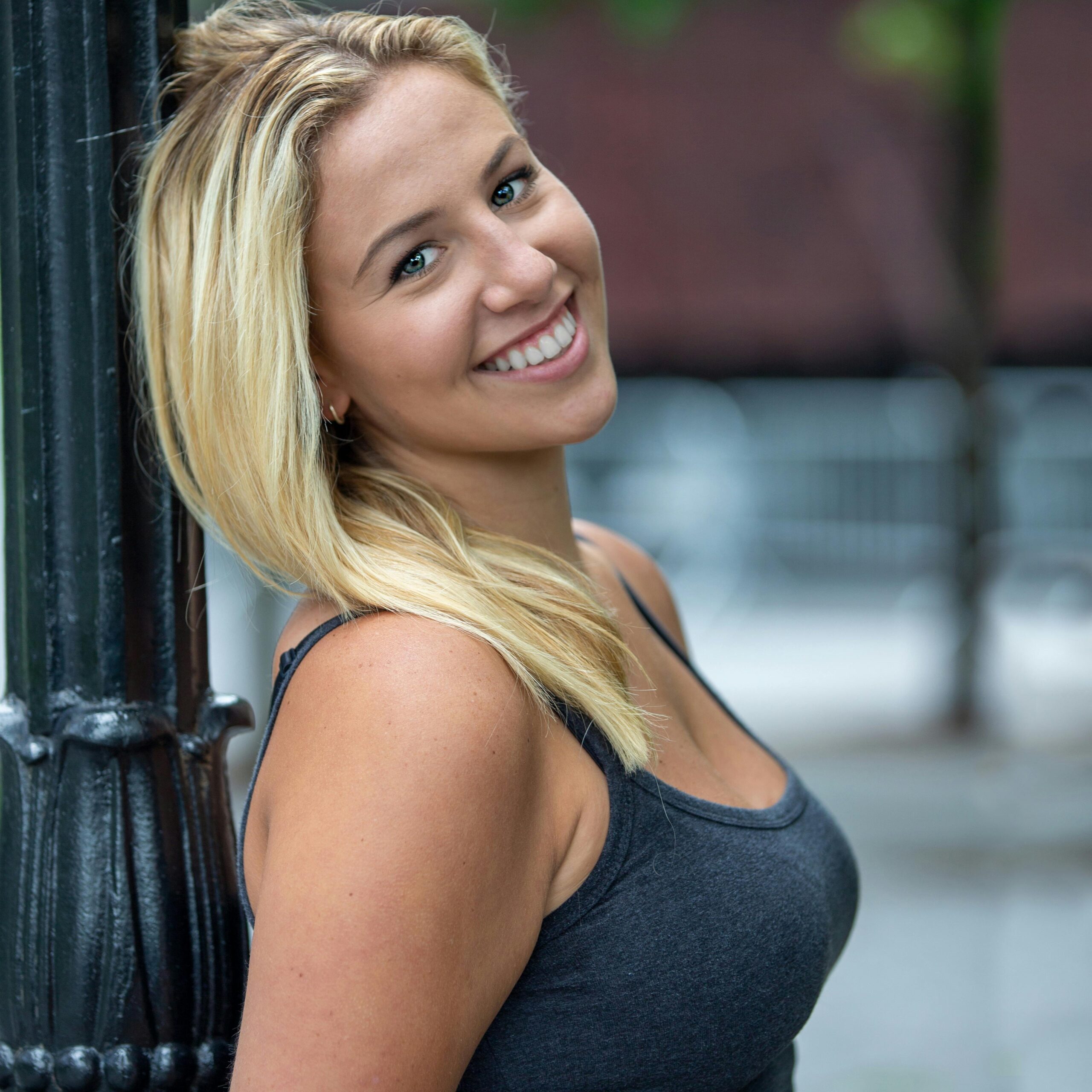 Portrait of a smiling woman leaning against a lamp post in New York City, capturing a candid and joyful moment outdoors.